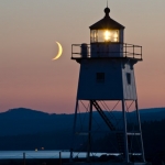 Lighthouse and Crescent Moon: A crescent moon rests near the Grand Marais lighthouse before it falls behind the Sawtooth Mountains.