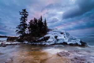 The sunrise turns the clouds purple and blue over an icy island on Lake Superior. Minnesota.