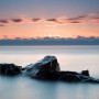 A small rocky island at Cascade River State Park during an early winter sunrise. Sea smoke dances on the horizon.